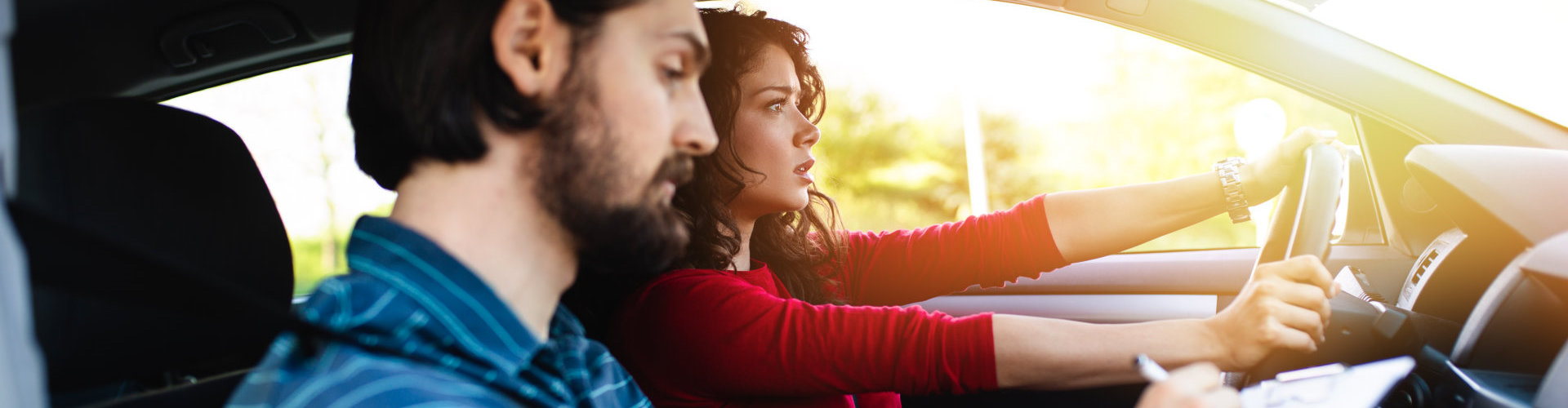 young woman learning how to drive car together with her instructor